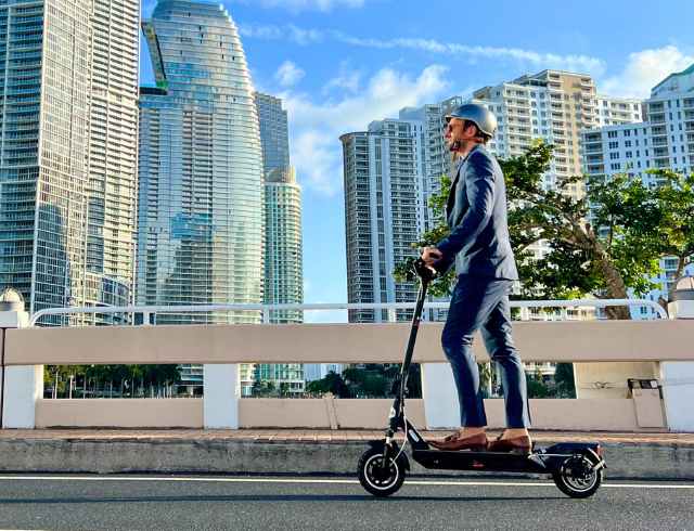 A man in suit and helmet riding electric scooter through city
