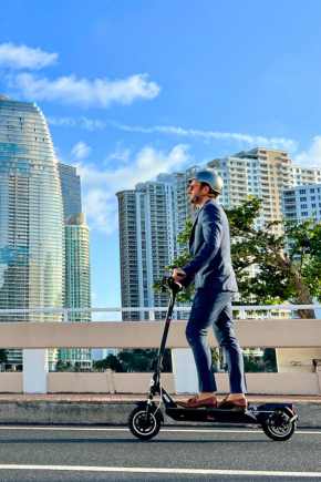 A man in suit and helmet riding electric scooter through city