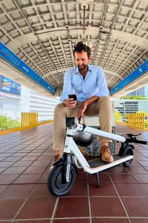 Man sitting in train station next to a folded escooter