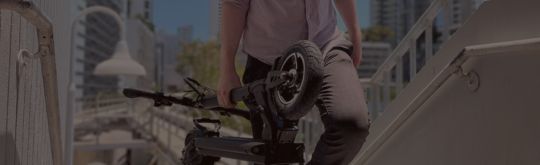Man carrying a folded electric scooter up stairs