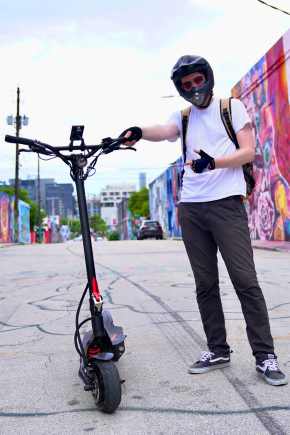 Man in helmet standing next to a fluidfreeride electric scooter