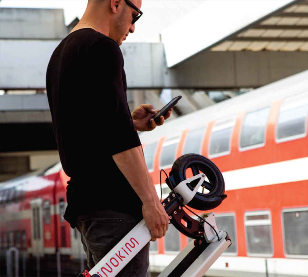 Commuter decoding the tech specs on his smartphone while holding a compact Inokim electric scooter, showcasing the blend of technology and modern transportation.