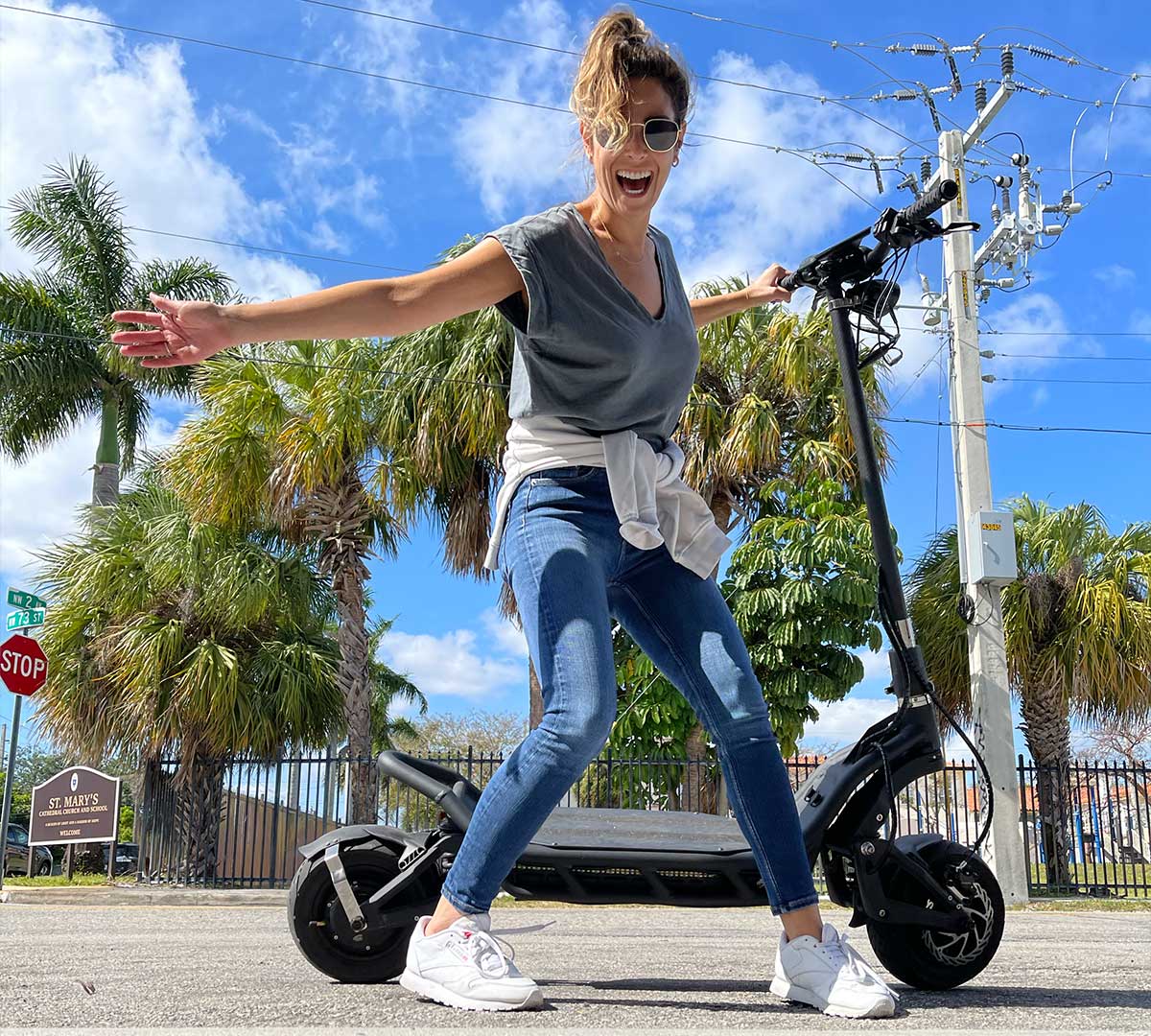 A woman expresses joy while balancing on an electric scooter, symbolizing the fun and eco-friendly benefits of electric mobility.