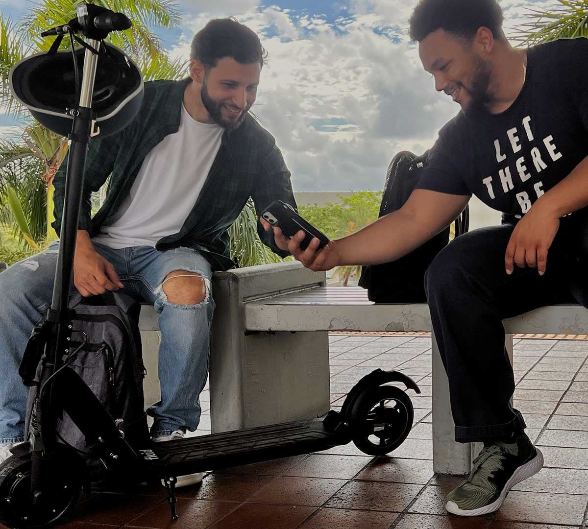 Two friends sharing the latest electric scooter apps while sitting on their scooters, representing a community of electric scooter enthusiasts.